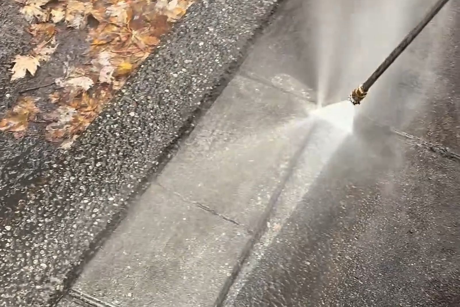 A fan of pressure washer spray cutting a clean line across a dirty concrete path