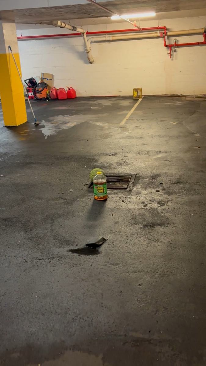 A wet parkade floor mid-wash with a round surface cleaner attachment sitting on the concrete