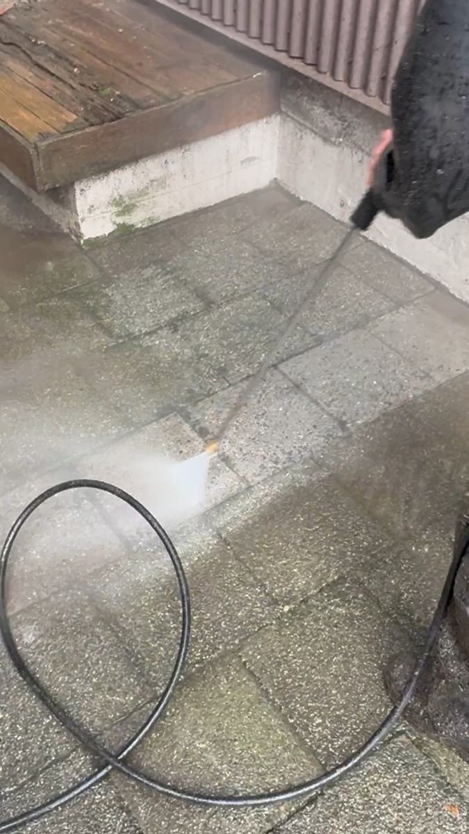 A pressure washer spraying a paver patio, the hose coiled on the section already washed
