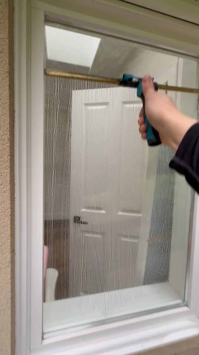 A squeegee cleaning the narrow glass panel beside a white front door