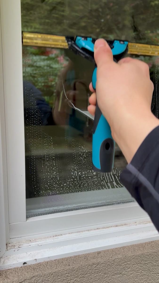 A squeegee pulled across a ground-floor window with a green garden visible through the glass