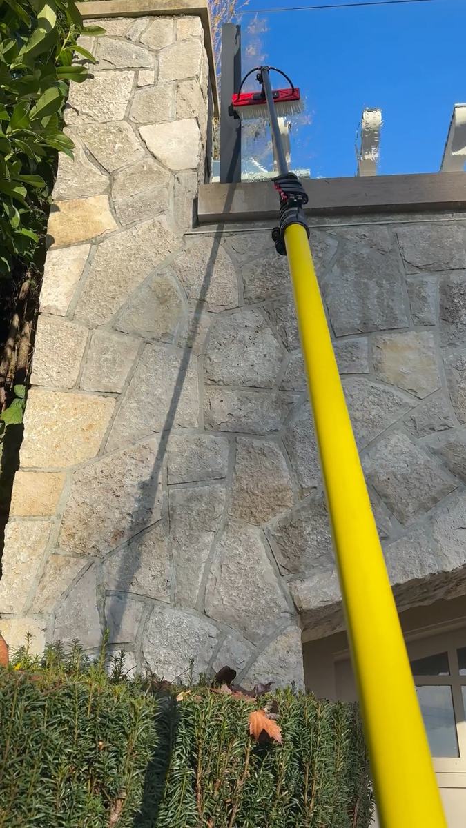 A yellow water-fed pole reaching up a stone wall to an upper window against a clear blue sky